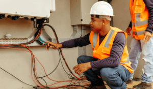Electrical workers inspecting wiring connected to an inverter system on a concrete wall.