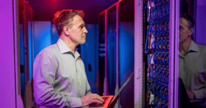 network engineer using a laptop to optimize business IT infrastructure in a data center aisle.