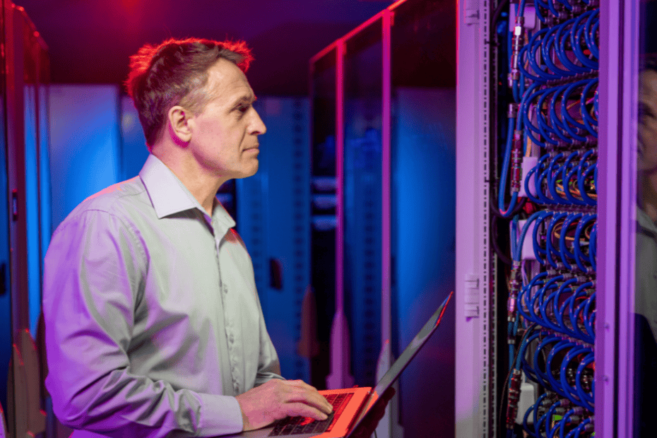 network engineer using a laptop to optimize business IT infrastructure in a data center aisle.